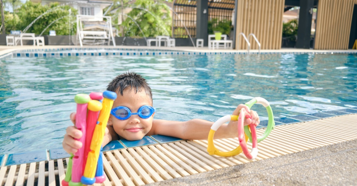 A child resting their chin on the edge of a pool while holding up the various diving toys they retrieved from the water. A child resting their chin on the edge of a pool while holding up the various diving toys they retrieved from the water.