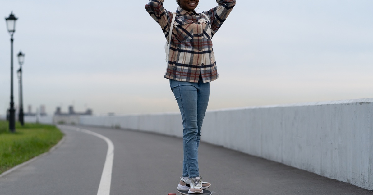 A person riding a skateboard down an outdoor road while wearing warm-weather clothing, including a jacket and beanie. A person riding a skateboard down an outdoor road while wearing warm-weather clothing, including a jacket and beanie.