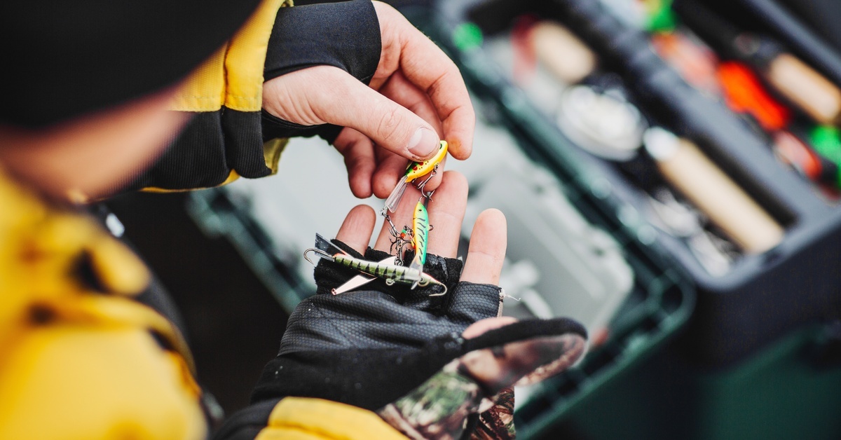 A person in cold-weather attire sorting through a handful of fishing lures shaped and painted to look like tiny fish.