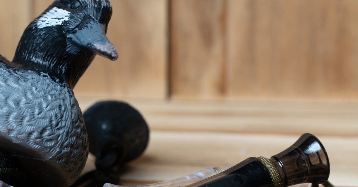 A black decoy duck sitting alongside old-school bird calls with paracord attachments to prevent them from getting lost.