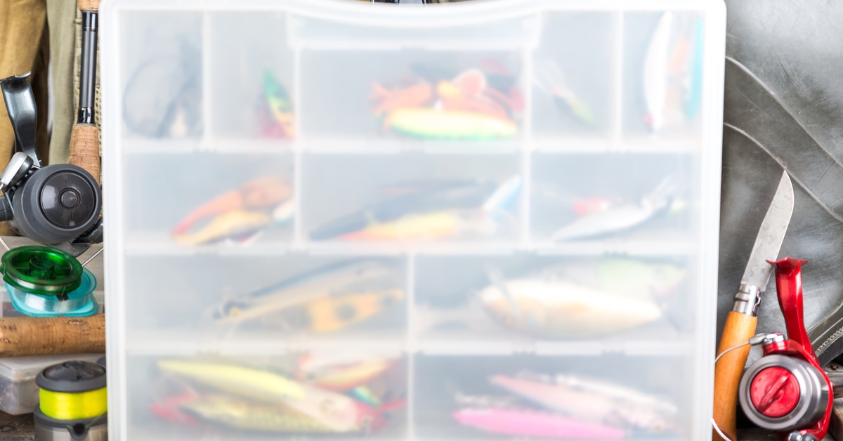 An assortment of colorful fishing lures visible behind the somewhat transparent lid of a full tackle sorting box.