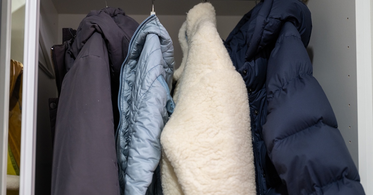 Four warm winter jackets of varying thicknesses hanging from a silver bar in a tightly-packed closet space.
