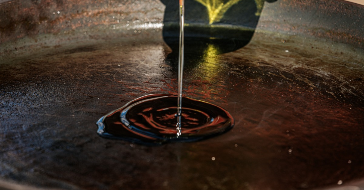 How To Season Cast Iron Properly for Nonstick Cooking A person drizzling a stream of oil onto the seasoned surface of a cast iron skillet that already has a light sheen.