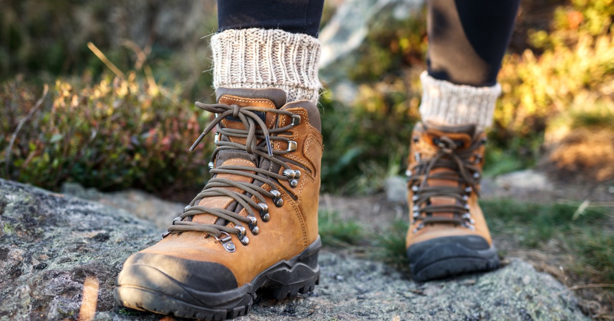 A close-up on a person's hiking books as they walk. They have knitted socks sticking out of the top of their boots.