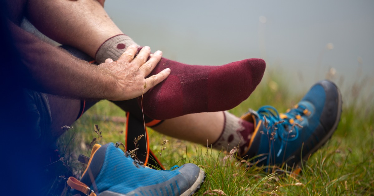 A hiker sitting on the ground to rest their feet. They've removed one of the boots and are touching their sock.