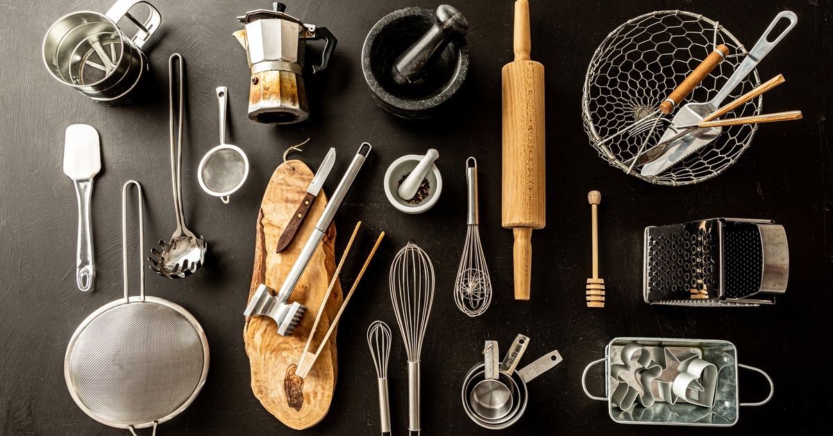 An assortment of unique kitchen tools, including a serving spade, meat tenderizer, French press, miller, whisks, and more.