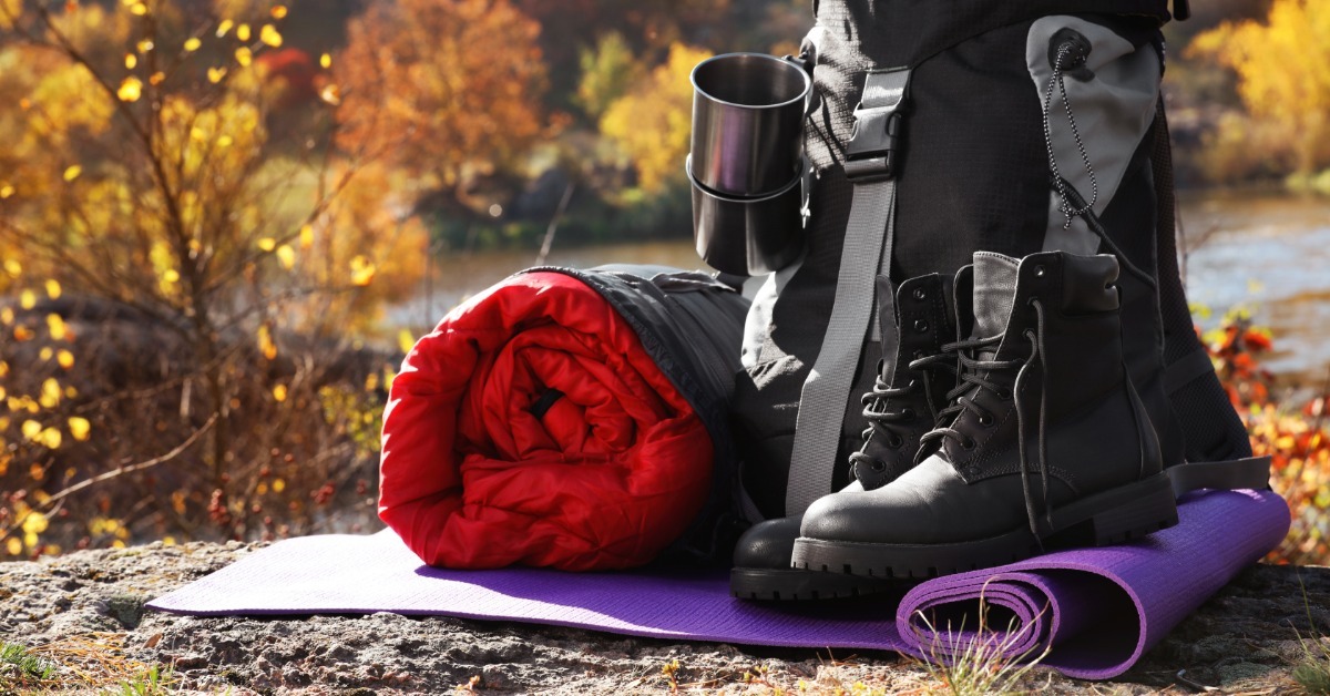 A compact backpack beside a compact, rolled sleeping bag and boots. The camping gear sits on a purple mat.