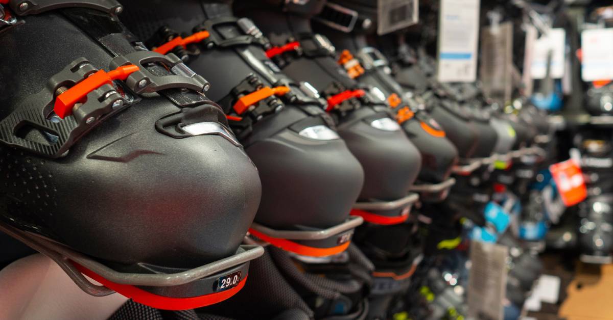 A close-up of a row of brand-new black ski boots for sale at a ski shop with more rows of boots above and below.