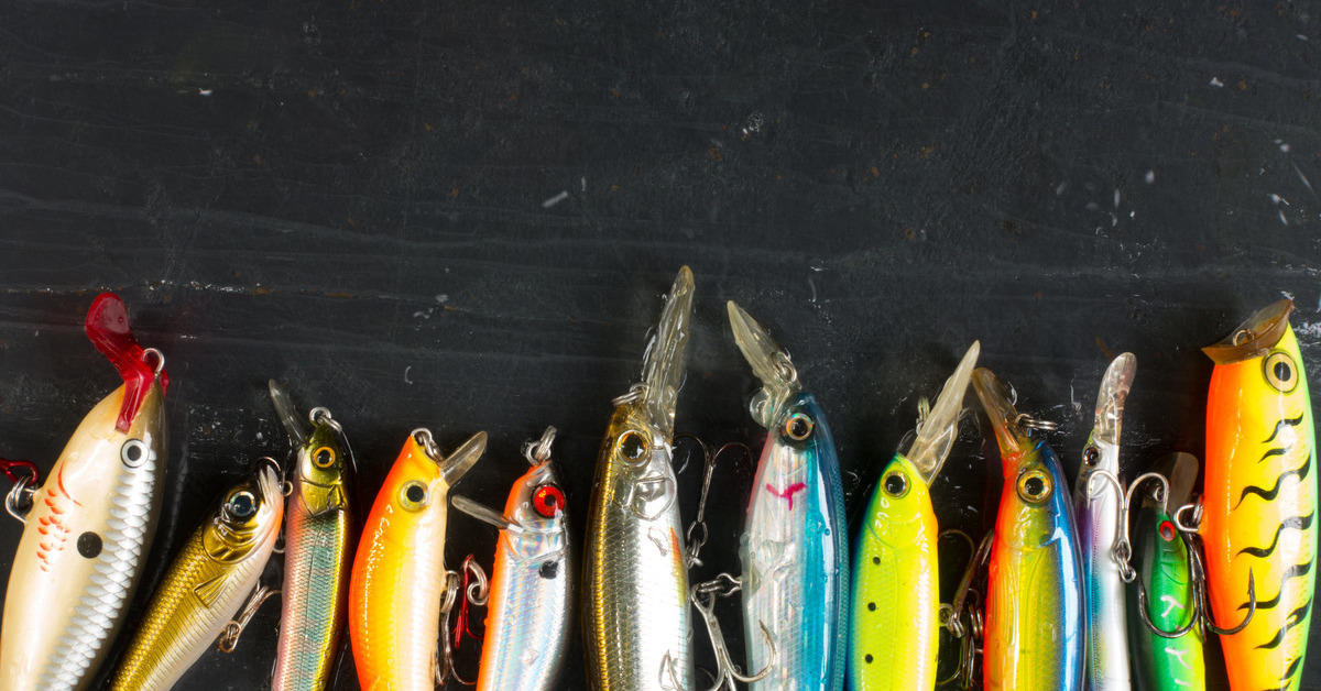 A close-up of various colored and sized fishing lures featuring hooks arranged in a line against a black background.