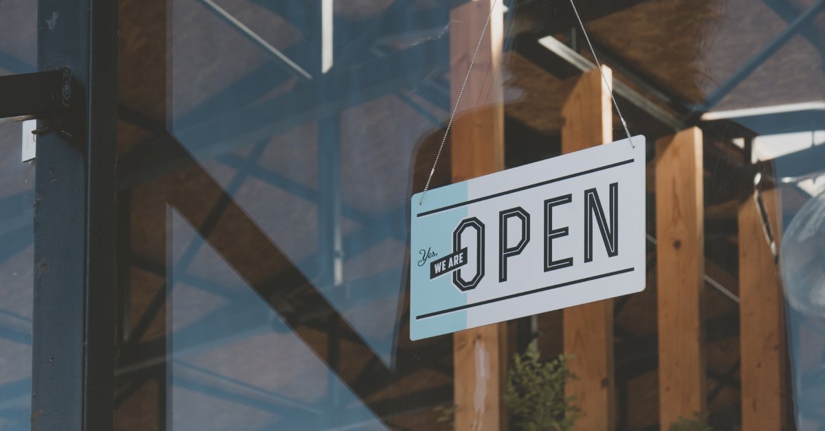 A close-up of a white sign hanging above a glass door in front of a business with the text, 