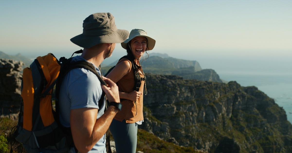 Two people wearing hats and standing and looking at each other. They smile and laugh with each other.