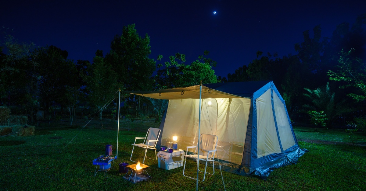 A camoing tent with an awning. There are two chairs under the awning. It is night time and stars are out.
