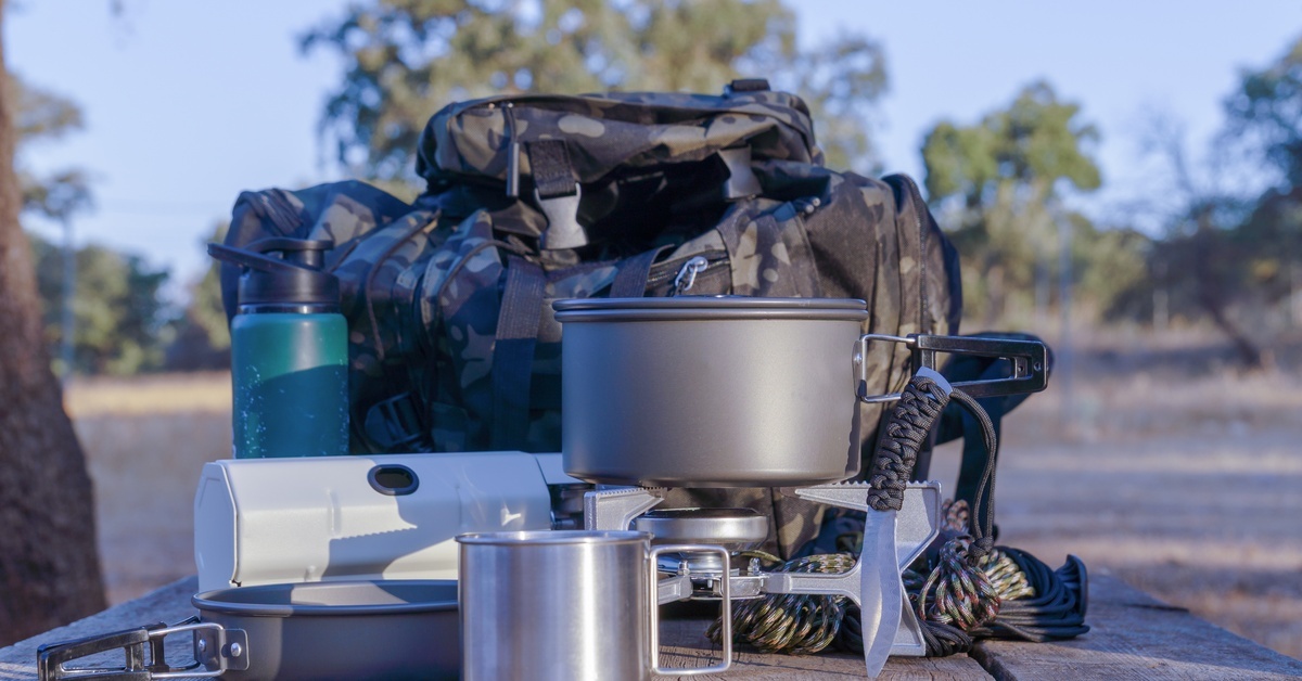 Various cooking utensils are sitting on a wooden surface. It’s outside and there is a tree in the background.