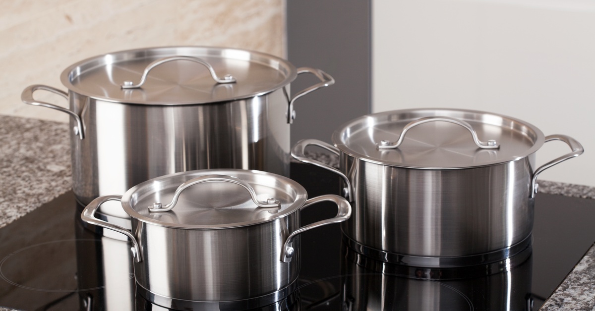 Three aluminum pots with matching lids sit on top of an induction stovetop. The counter is gray with specks of black.