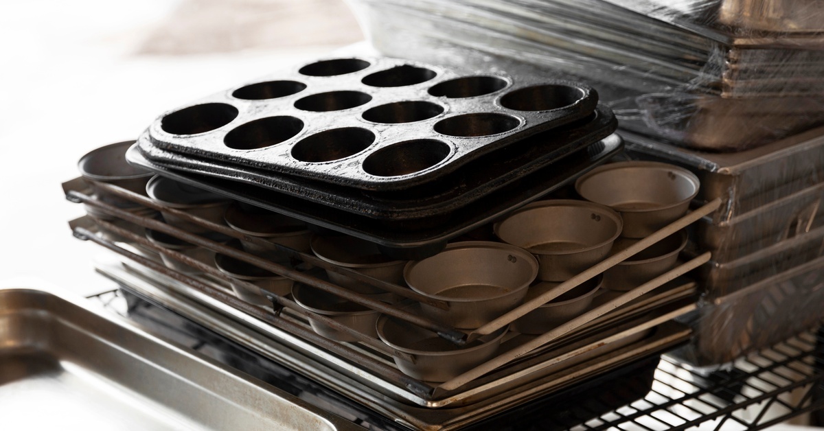 A stack of metal baking pans sitting on a wire rack. Different sizes of cupcake tins are in the stack.