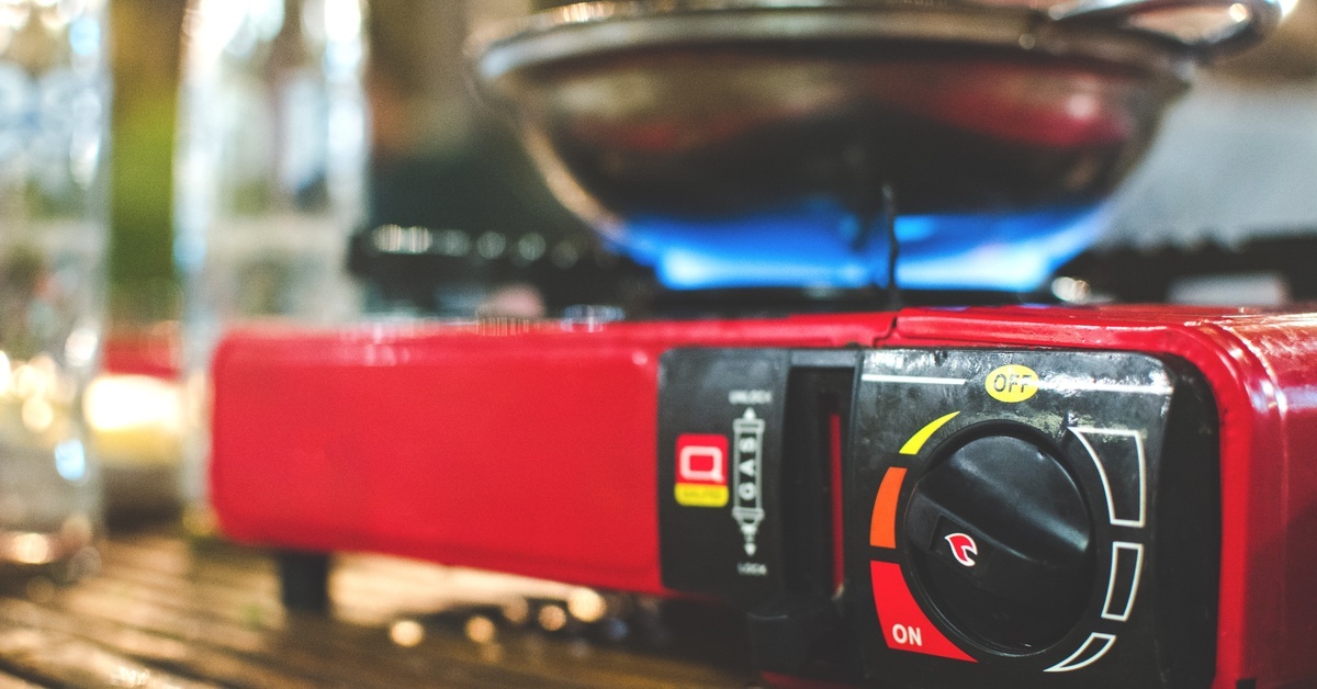 A silver pan sitting on a lit portable stove inside a building. The dial on the stove is set on medium heat.