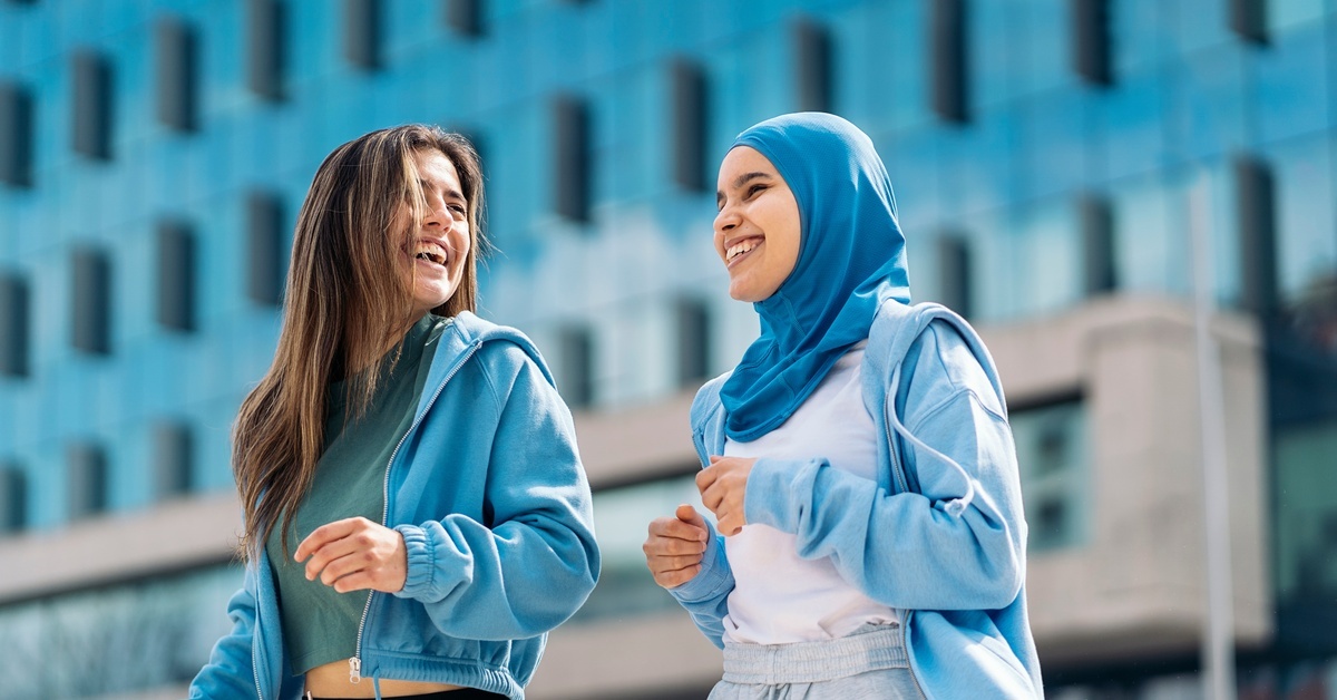 Two women walking in front of a tall building. They are both wearing loose, activewear clothes and smiling.